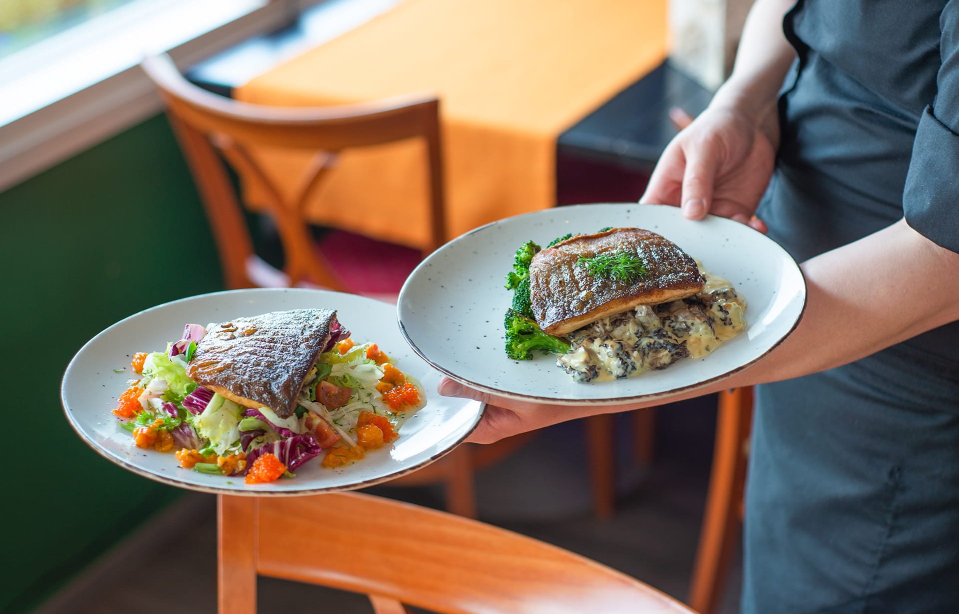 Ravintola | Ravintola Punakettu Tarjoilija kantaa kahta kala-annosta pöytään.